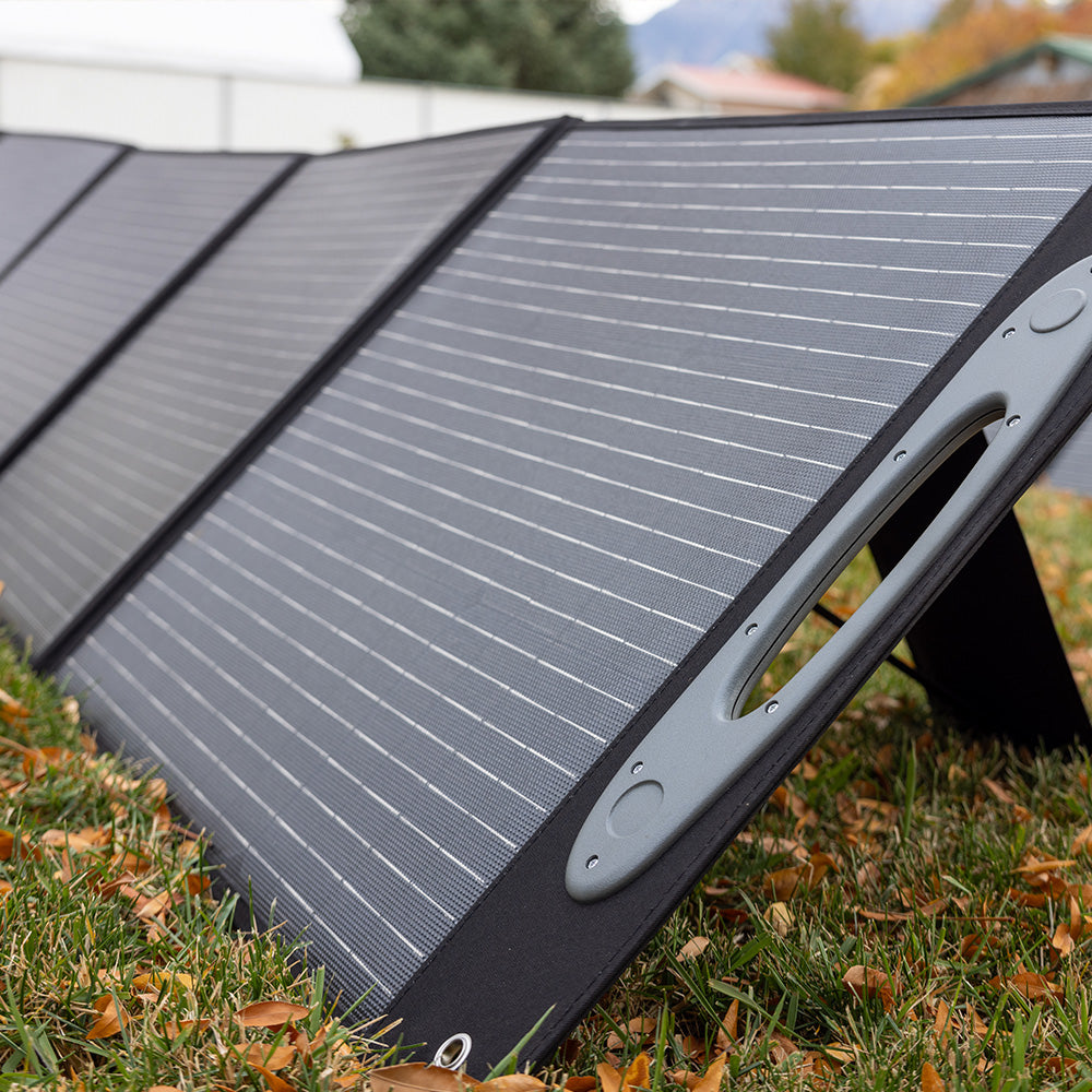 Photograph of a 200W monocrystalline solar panel with a sleek, dark surface and aluminum frame, part of the Grid Doctor 3300 Solar Generator System, on a grassy background.
