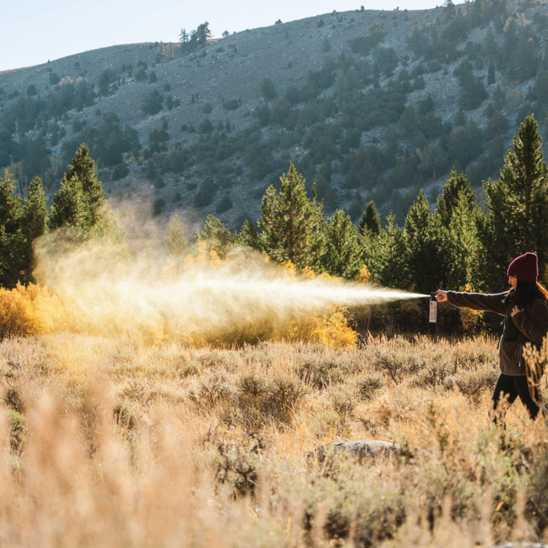 A woman deploying bear spray from a far distance in a mountainous environment.