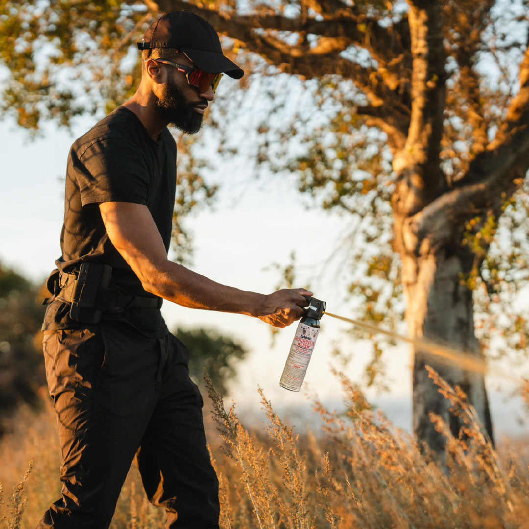 A man deploying bear spray in a grassy environment with trees.