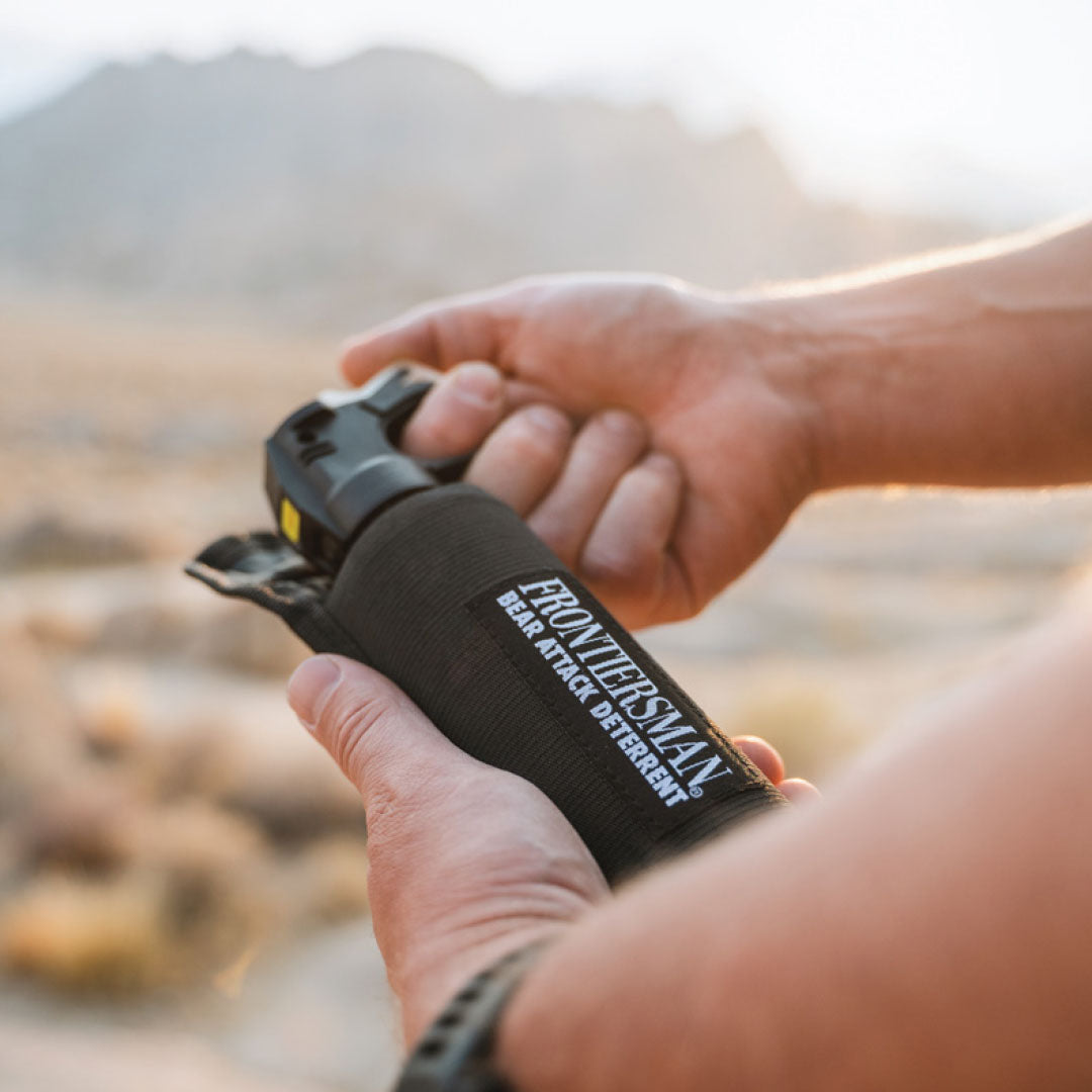 A man holding a canister of bear spray in a wild desert environment.