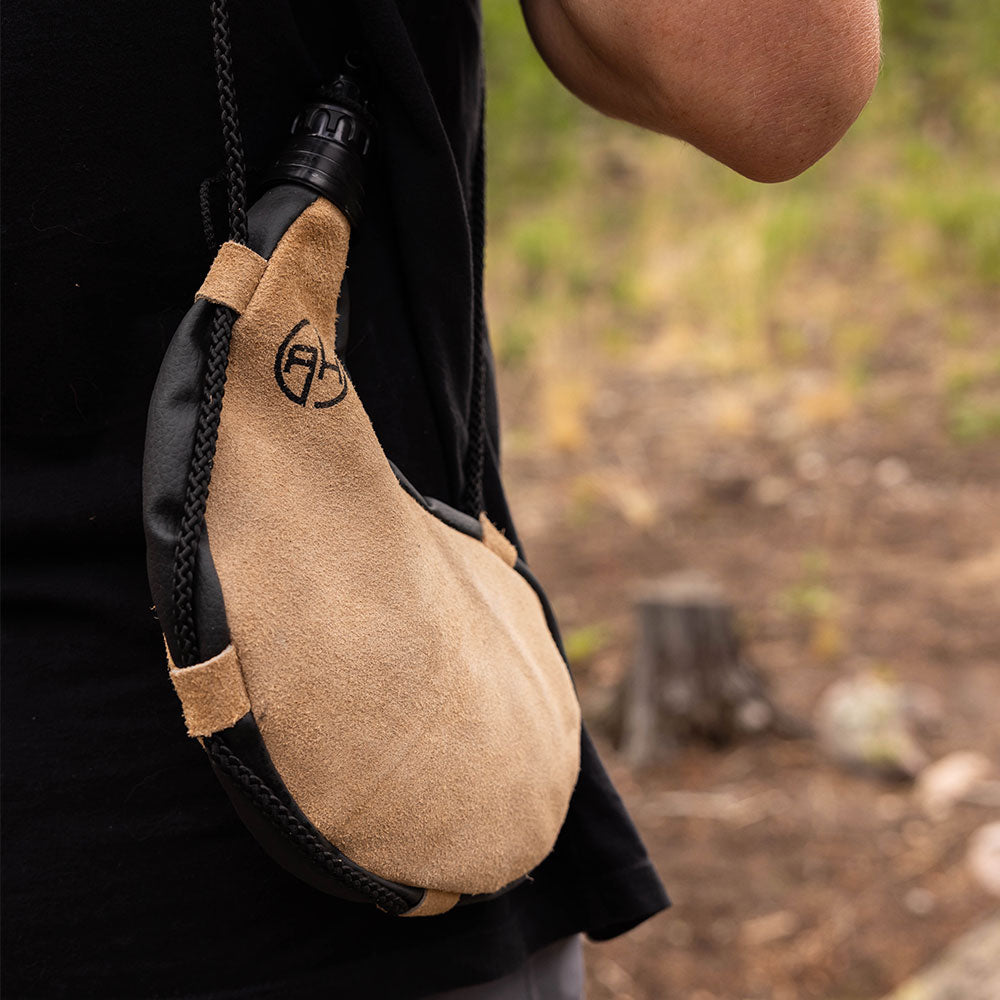 Man wearing a tan leather bota bag on his side outdoors.