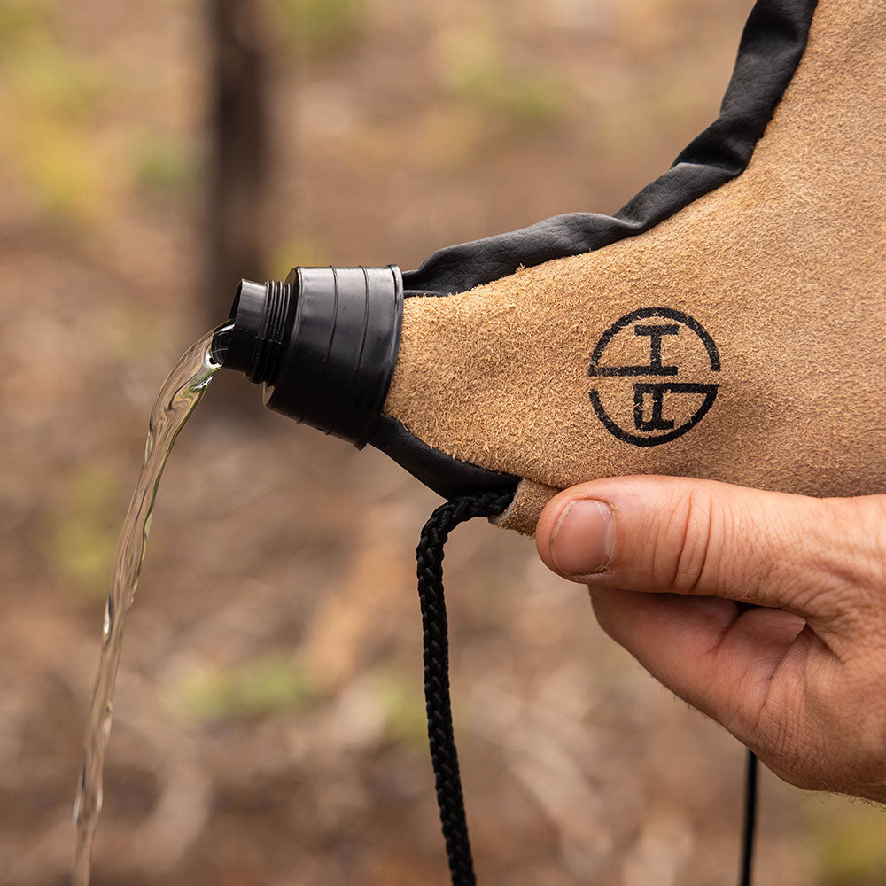 Man pouring water out of a tan leather canteen pouch outdoors.