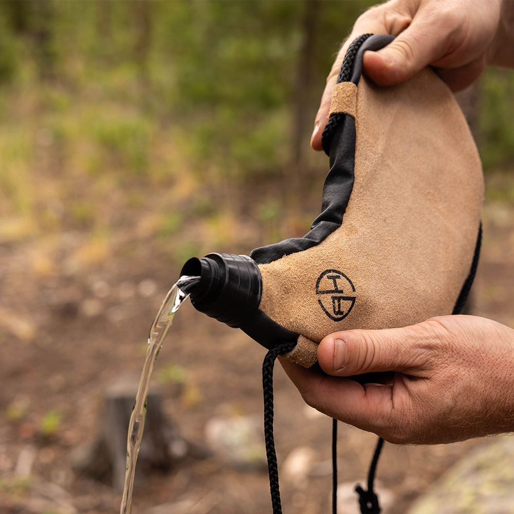 Man tipping over and pouring the water out of a canteen pouch outdoors.