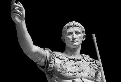 An ancient Roman statue in white standing against a black background.