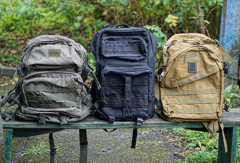 Three different nondescript backpacks lined up on a bench in different colors.