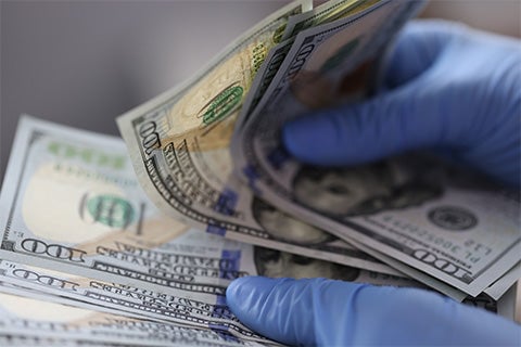 A person with blue latex gloves counting large amounts of money.