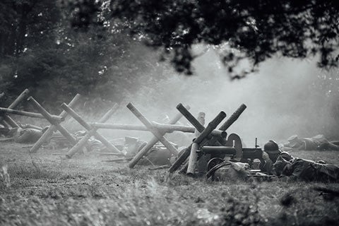 A barricade on a battlefield with soldiers lying beneath it in wait with their weapons.