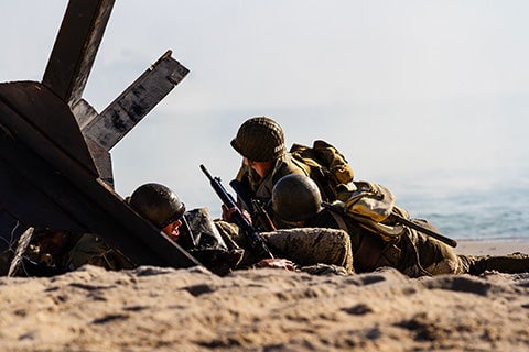 Soldiers huddled on a sandy beach in full combat gear.