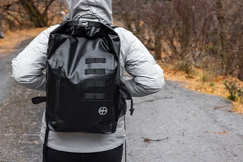 A person wearing a gray hoodie carrying a Waterproof EMP Faraday Backpack on their back walking up a hill.
